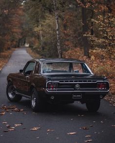 an old car is parked on the side of the road in front of some trees