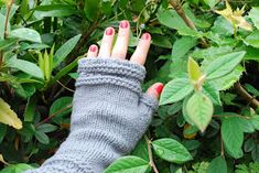 a woman's hand wearing a gray knitted arm warmer in front of green leaves