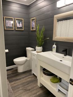 a white toilet sitting next to a sink in a bathroom under two framed pictures on the wall