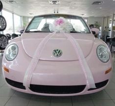 a pink vw beetle parked in front of a car with a bouquet of flowers on the hood