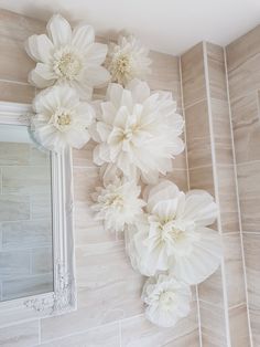 three white flowers are hanging on the wall next to a mirror