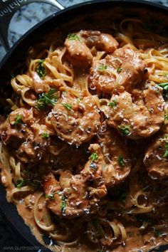 a skillet filled with pasta and meat covered in gravy, garnished with parsley