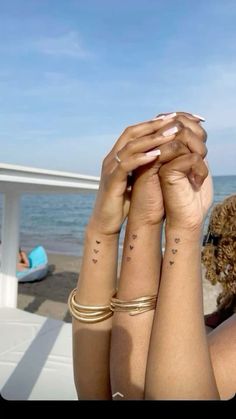 two women with matching tattoos on their arms holding each other's hands near the ocean