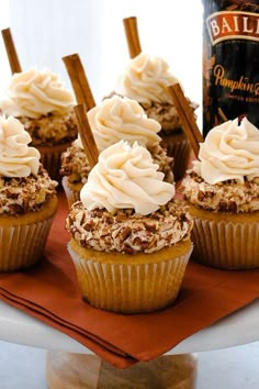 cupcakes with white frosting and cinnamon sticks on a plate next to a bottle of bailey's