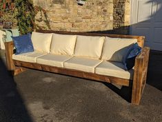 a wooden couch sitting in front of a brick building with pillows on it's back