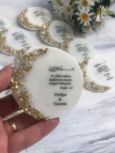 a person holding a white plate with gold trimmings on it and some flowers in the background