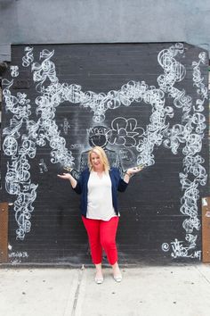 a woman standing in front of a black wall with white flowers and vines on it