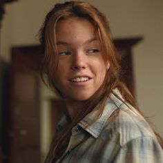 a woman with long red hair is smiling for the camera while wearing a plaid shirt