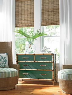 a green dresser sitting in front of a window next to two chairs and a plant