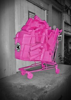 a pink shopping cart filled with lots of items sitting on the side of a building