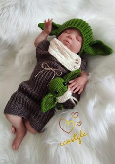 a baby wearing a knitted yoda outfit laying on top of a white blanket