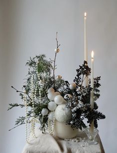 a white vase filled with christmas decorations next to two lit candles on top of a table