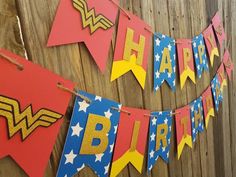 a birthday banner with the words happy birthday written on it and wonder woman decorations hanging from a wooden fence