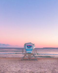 a lifeguard chair sitting on top of a sandy beach next to the ocean at sunset