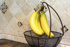 two bananas are sitting in a wire basket on the kitchen counter next to a tile backsplash