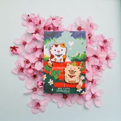 there is a book with cats on it surrounded by pink flowers