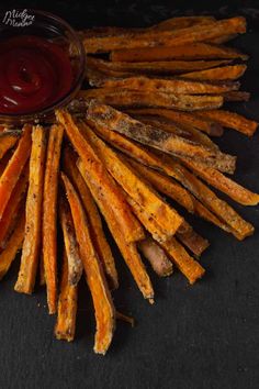 french fries with ketchup are arranged on a black surface