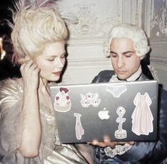 a man and woman sitting next to each other looking at a laptop screen with stickers on it