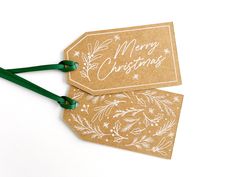 two brown tags with green handles are on a white surface and one has the words merry christmas written on it