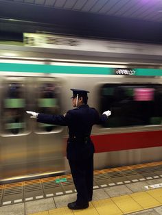 a man in uniform standing next to a train at a subway station with his arms outstretched