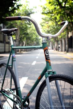 a green bicycle parked on the side of a road next to trees and buildings in the background