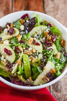 a salad with apples and cranberries in a white bowl on a wooden table