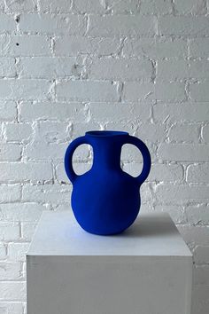 a blue vase sitting on top of a white block in front of a brick wall