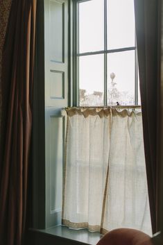 a window with curtains and a chair in front of it, looking out the window