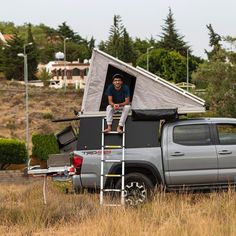 a man sitting on top of a truck with a tent attached to it's roof