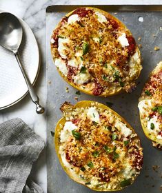 three stuffed peppers with cheese and herbs on a baking sheet next to a spoon, fork and napkin