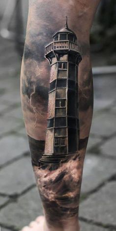 a man's leg with a lighthouse tattoo on it and clouds in the background