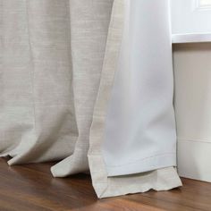 the side of a curtain in front of a window with wood flooring and white curtains