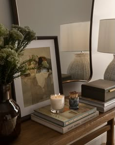 a wooden table topped with books and a vase filled with flowers next to a mirror