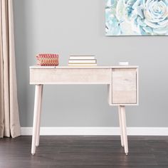 a white desk with books on it in front of a painting and window sill