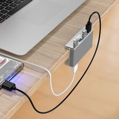 an electronic device connected to a laptop on a wooden desk with a charger plugged in