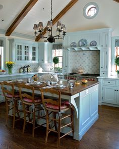 a large kitchen with an island and wooden chairs in the center, surrounded by white cabinets