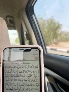 a person holding up a cell phone in their hand while sitting in a car with the driver's seat open