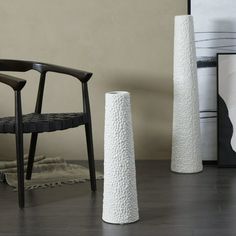 three tall white vases sitting on top of a wooden floor next to a chair