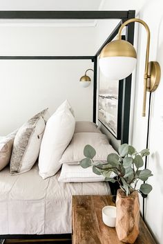 a bed with white sheets and pillows next to a plant