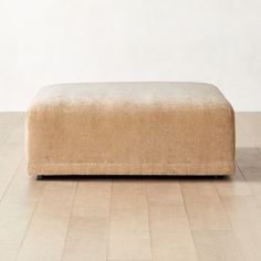 a tan ottoman sitting on top of a hard wood floor next to a white wall