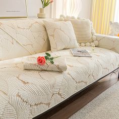 a white couch covered in pillows and blankets with a rose laying on top of it