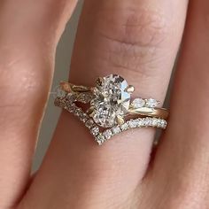 a woman's hand with two wedding rings on top of her finger and the ring has an oval shaped diamond surrounded by smaller round diamonds