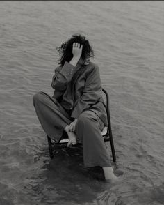 a woman sitting on a chair in the water with her hand to her face while talking on a cell phone