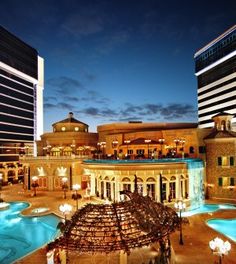 an outdoor swimming pool in the middle of a city at night with lights on it