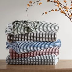 a stack of towels sitting on top of a wooden table next to a vase with flowers