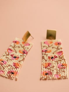 a pair of beaded earrings sitting on top of a pink table next to each other