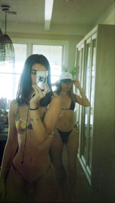 two beautiful women in bikinis taking pictures with their cell phones while standing next to each other