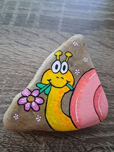 a painted rock with a yellow snail holding a pink flower on it's side