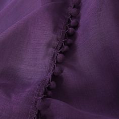 purple fabric with pom - poms on the bottom and side, close up