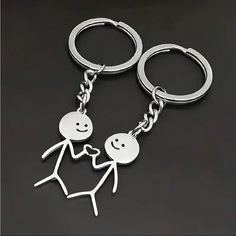 two metal key chains that are shaped like people holding each other's hands and smiling